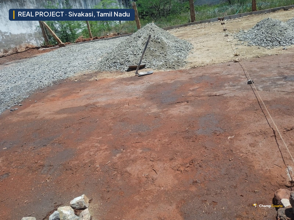 Bare red-earth plot in Sivakasi set out with string lines, stockpiles of grey aggregate along the boundary wall before b