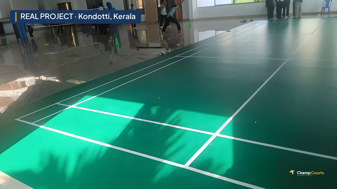 Sunlight across the finished vinyl badminton court at Blossom Arts and Science College, Kondotti, with students playing badminton by the net at the far end of the hall
