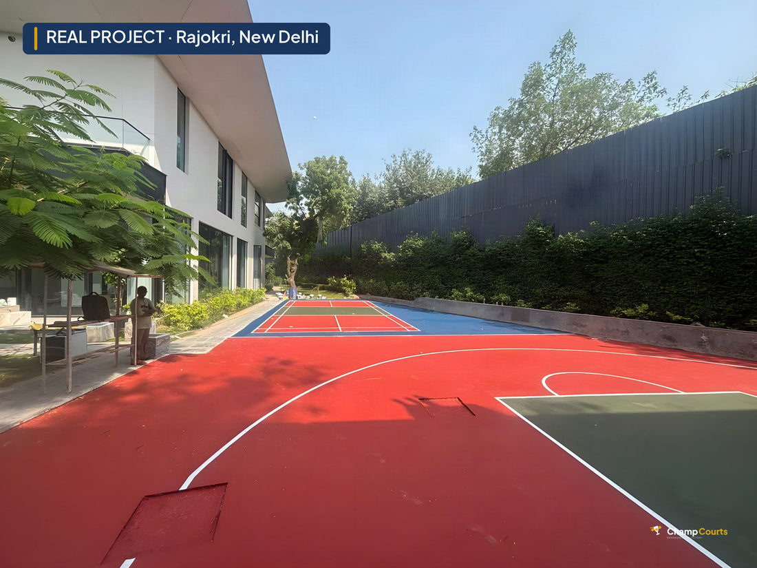 Long daylight view down the finished red acrylic court in Rajokri, New Delhi, with the house on the left and the hedge-lined boundary on the right