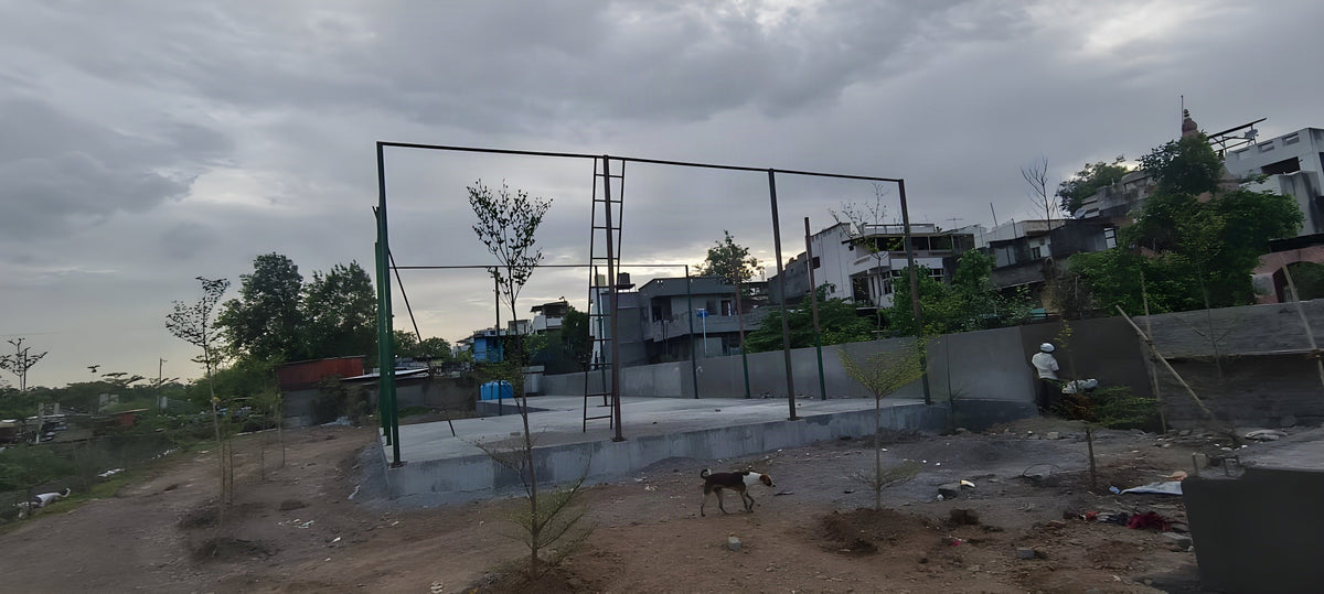 Steel enclosure framework being erected on the finished grey concrete platform at the Chalisgaon riverfront complex, bef