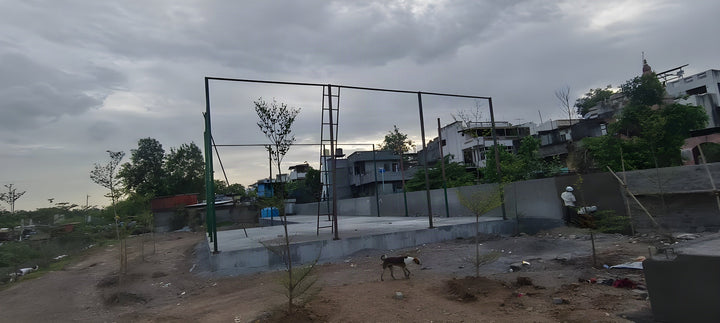 Steel enclosure framework being erected on the finished grey concrete platform at the Chalisgaon riverfront complex, bef