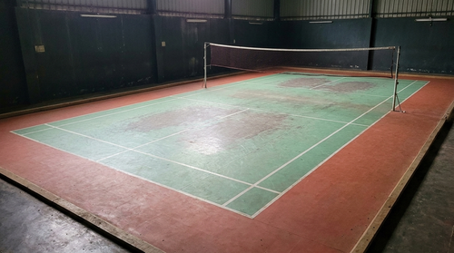 Worn, faded badminton court before renovation, with cracked acrylic and washed-out lines (visualization)
