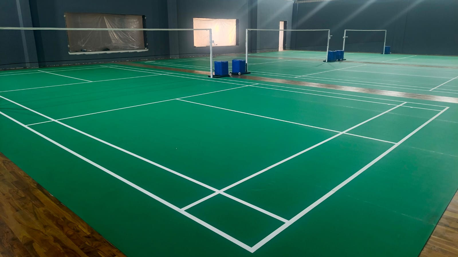 Indoor badminton hall with green PVC mat courts laid over a teak sprung wooden floor